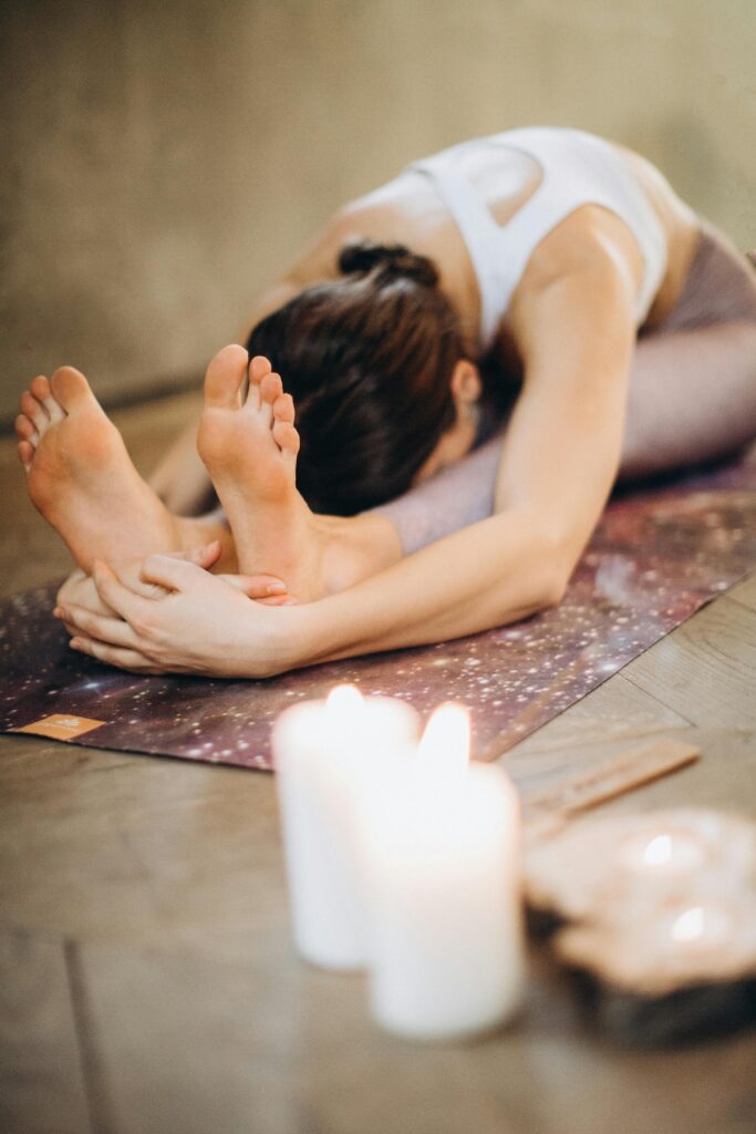 Woman practicing yoga in a seated forward bend with candles for relaxation and mindfulness.